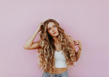 Woman with long curly blonde hair standing in front of a pink wall